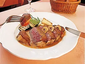 岡の店内、テーブルの上には肉料理とワイン、パンの写真